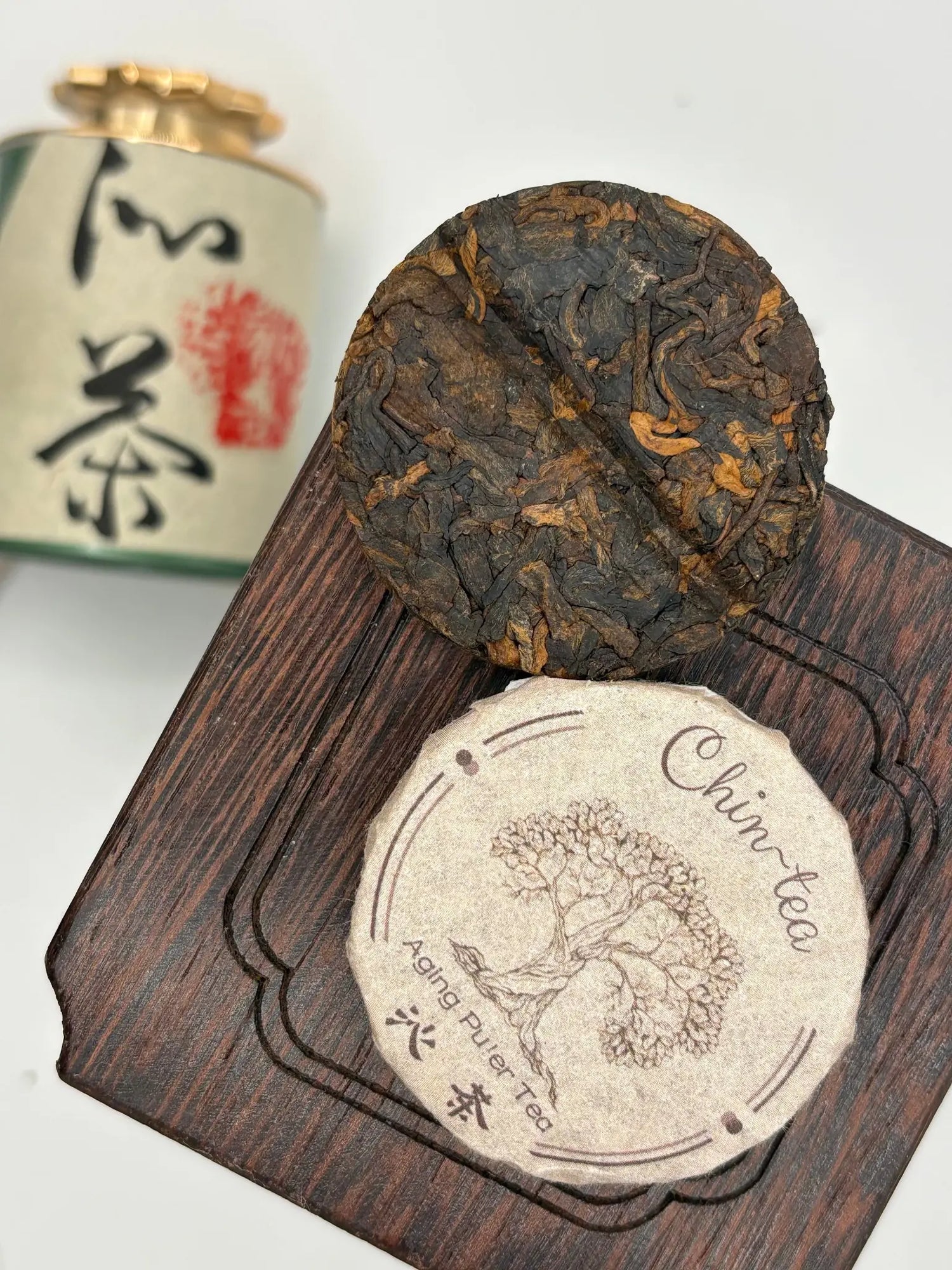 Aged Pu'er tea cake from Chin-Tea Studio displayed on a wooden tea tray, showcasing compressed fermented tea leaves from Yunnan, China.